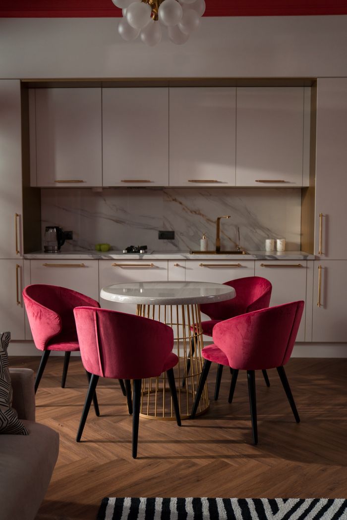 The Art of Drawing Readers In: Your attractive post title goes here Cozy kitchen interior with pink velvet chairs, a round table, and modern cabinetry.